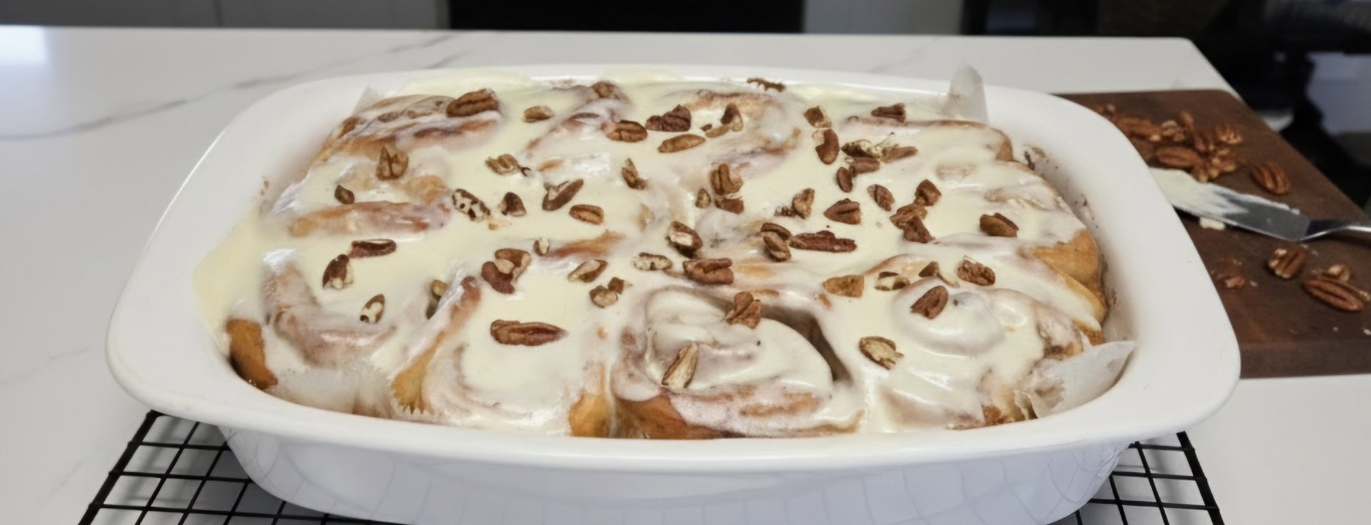 A dish of frosted cinnamon rolls topped with pecans